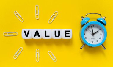 Finans ve ekonomi kavramı. Sarı arkaplanda, mavi alarm saati, ataçlar ve metnin yazıldığı beyaz küpler - VALUE