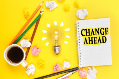 İş ve teknoloji kavramı. Sarı arka planda, bir fincan kahve, bir ampul, kalemler, üzerinde yazı olan bir defter.