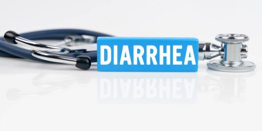 Tıp ve sağlık konsepti. Beyaz yansıtıcı yüzeyde bir stetoskop ve üzerinde DiARRHEA yazılı mavi bir Jenga var.