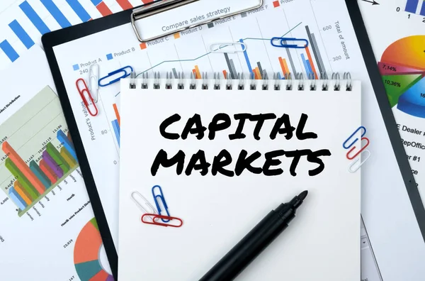 Business and finance. On the table are reports, charts, a notebook with the inscription - CAPITAL MARKETS