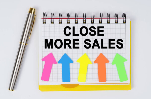 Business and finance concept. On a white background lie a pen and a notebook with the inscription - CLOSE MORE SALES