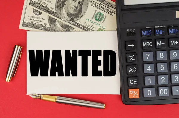 Business and finance concept. On a red background, among the money, a calculator and a pen lies a sign with the text - WANTED