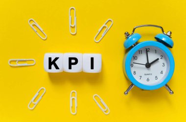 Finans ve ekonomi kavramı. Sarı arkaplanda, mavi alarm saati, ataçlar ve metnin yazıldığı beyaz küpler - KPI
