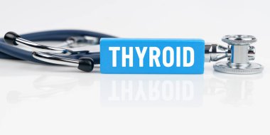 Tıp ve sağlık konsepti. Beyaz yansıtıcı yüzeyde bir stetoskop ve üzerinde THYROID yazan mavi bir Jenga var.