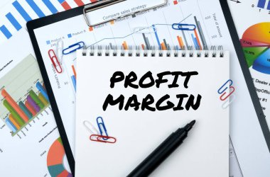 İş ve finans. Masanın üzerinde raporlar, çizelgeler ve içinde PROFIT MARGIN yazan bir defter var.