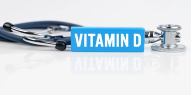 Tıp ve sağlık konsepti. Beyaz yansıtıcı yüzeyde bir stetoskop ve üzerinde VITAMIN D yazılı mavi bir Jenga bulunur.