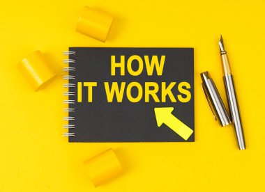 İş ve finans kavramı. Sarı bir arka planda bir kalem, üzerinde nasıl çalıştığı yazılı siyah bir defter bulunur.