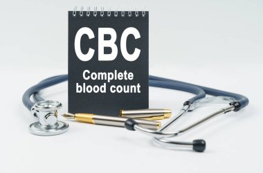 Tıp ve sağlık konsepti. Beyaz arka planda bir stetoskop, bir kalem ve üzerinde kan sayımı yazılı siyah bir defter bulunur.