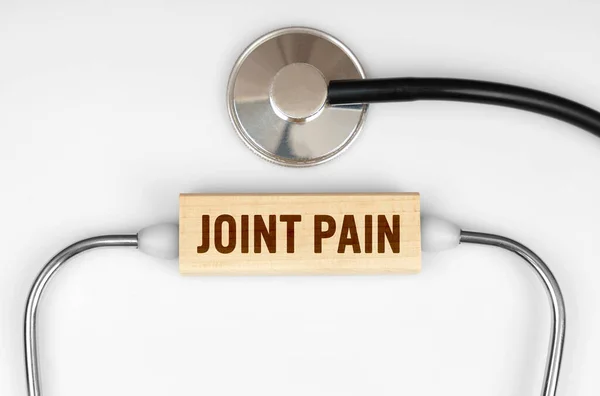 Health and medicine concept. On the table is a stethoscope and a wooden plate with the inscription - JOINT PAIN