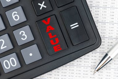 İş ve finans. Masanın üzerinde bir rapor, bir kalem ve hesap makinesi var, büyük tuşun üzerinde VALUE yazıyor.