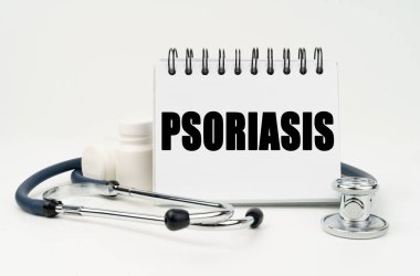 Tıp ve sağlık konsepti. Beyaz bir masada steteskop, haplar ve üzerinde PSORIASIS yazan bir defter var.