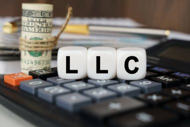 Business and finance concept. There are cubes on the calculator that say - LLC. Nearby out of focus - dollars, notebook and pen clipart