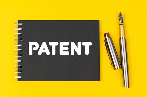 商业和金融概念 在黄色的背景上 有一支笔和一个黑色的笔记本 上面写着专利 — 图库照片