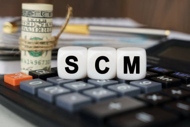 İş ve finans kavramı. Hesap makinesinde SCM yazan küpler var. Yakınlarda odak dışı - dolar, defter ve kalem