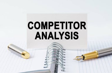 Finans ve iş konsepti. Masanın üzerinde bir defter, bir kalem ve üzerinde COMPETITOR ANALYSIS yazan bir kartvizit var.