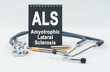 Tıp ve sağlık konsepti. Beyaz arka planda bir steteskop, bir kalem ve üzerinde ALS yazılı siyah bir defter bulunur.