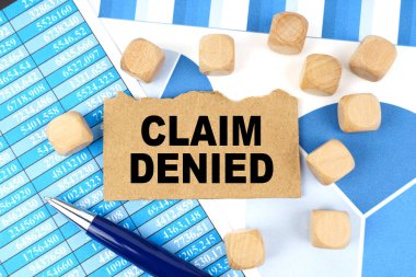 Finans ve ekonomi. Grafikleri ve raporları olan belgelerde, üzerinde CLAIM DENIED yazan küpler ve kartonlar var.