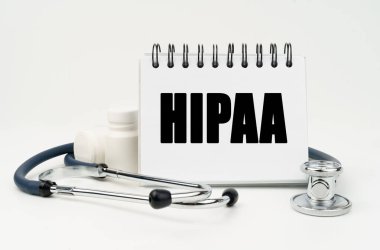 Tıp ve sağlık konsepti. Beyaz bir masada steteskop, haplar ve üzerinde HIPAA yazan bir defter var.