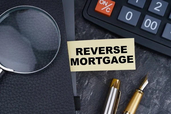 Finans ve iş konsepti. Masanın üzerinde bir hesap makinesi, bir kalem, bir büyüteç ve üzerinde kitap ayracı olan bir defter var - REVERSE MORTGAGE