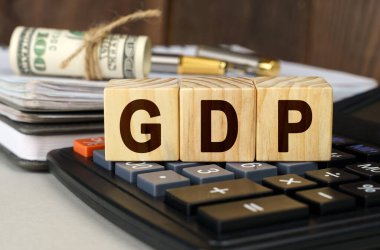 Finans ve ekonomi kavramı. Masanın üzerinde para, hesap makinesi, bir defter ve üzerinde GSYİH yazan küpler var.