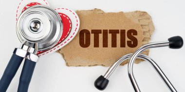Tıp ve sağlık konsepti. Beyaz bir masada bir kalp, bir steteskop ve üzerinde otitis yazılı bir karton bulunur.