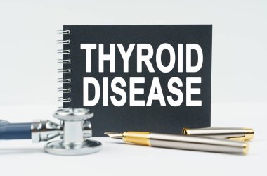 Tıp ve sağlık konsepti. Beyaz arka planda bir stetoskop, bir kalem ve üzerinde THYROID hastalığı yazan siyah bir defter bulunur.