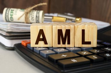 Finans ve ekonomi kavramı. Masanın üzerinde para, hesap makinesi, bir defter ve üzerinde AML yazan küpler var.