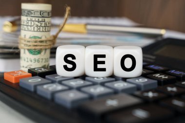 Business and finance concept. There are cubes on the calculator that say - SEO. Nearby out of focus - dollars, notebook and pen
