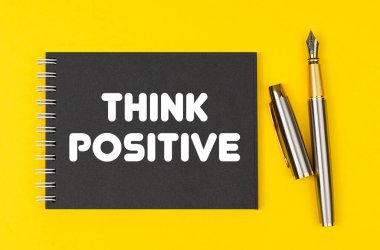 Business and finance concept. On a yellow background lies a pen and a black notebook with the inscription - Think Positive