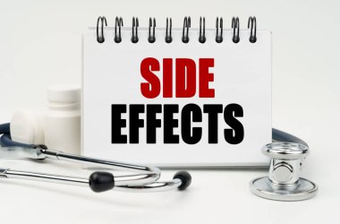 Medicine and health concept. On a white table lies a stethoscope, pills and a notebook with the inscription - SIDE EFFECTS