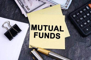 Finance and business concept. On the table is a calculator, a pen, money and stickers with the inscription - MUTUAL FUNDS