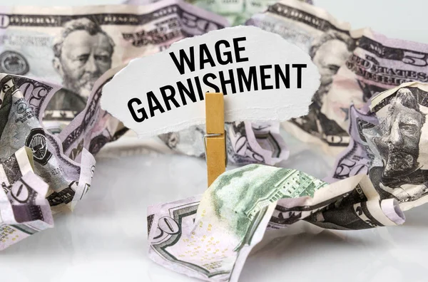 Business and finance concept. There are dollars on the table and there is a clothespin with paper on which it is written - WAGE GARNISHMENT