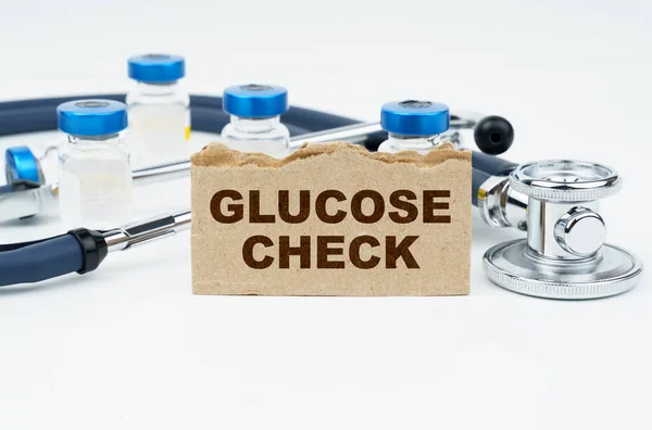 医学和健康概念 在一张白色的桌子上躺着安培 一个听诊器和一个印有题词的纸板 Glucose Check — 图库照片
