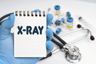 Tıp konsepti. Masanın üzerinde steteskop var, doktor elinde X-ray yazılı bir defter tutuyor.