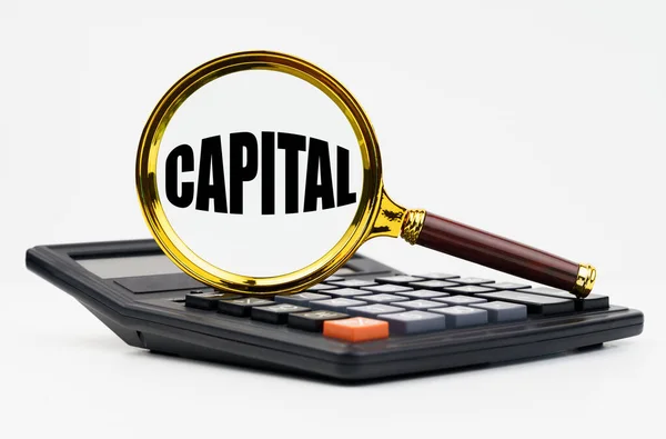 金融和商业概念 白色背景上有一个计算器和一个刻有 Capital 字样的放大镜 — 图库照片