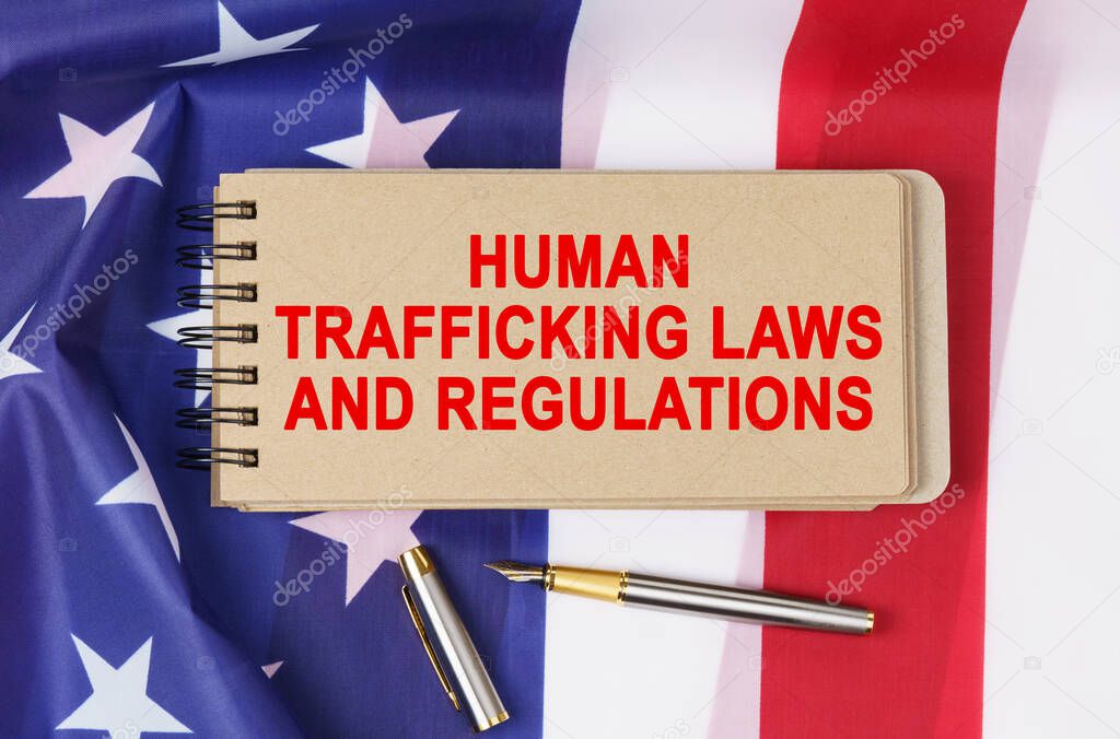 Law and order concept. Against the background of the flag of the United States of America lies a notebook with the inscription - HUMAN TRAFFICKING LAWS AND REGULATIONS