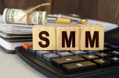 Finans ve ekonomi kavramı. Masanın üzerinde para, hesap makinesi, bir defter ve üzerinde SMM yazan küpler var.