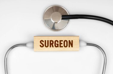 Sağlık ve tıp konsepti. Masanın üzerinde steteskop ve üzerinde SURGEON yazan ahşap bir tabak var.