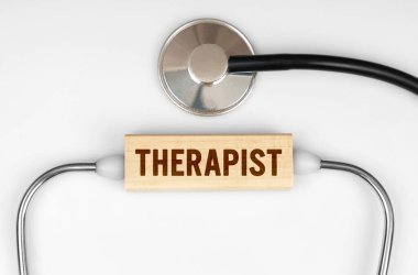 Sağlık ve tıp konsepti. Masanın üzerinde bir steteskop ve üzerinde THERAPIST yazan ahşap bir tabak var.