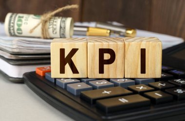 Finans ve ekonomi kavramı. Masanın üzerinde para, hesap makinesi, bir defter ve üzerinde KPI yazan küpler var.