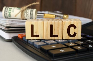 Finans ve ekonomi kavramı. Masanın üzerinde para, hesap makinesi, bir defter ve üzerinde LLC yazan küpler var.