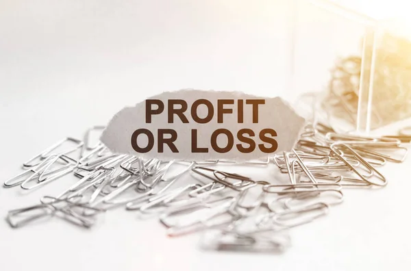 Business and finance concept. Paper clips are scattered on the table and there is paper with the inscription - PROFIT OR LOSS