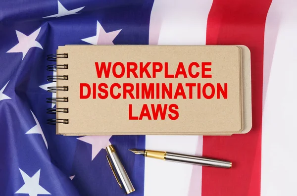 Law and order concept. Against the background of the flag of the United States of America lies a notebook with the inscription - WORKPLACE DISCRIMINATION LAWS