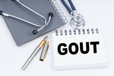 Tıp ve sağlık konsepti. Masanın üzerinde steteskop, kalem ve üzerinde gut yazan bir defter var.