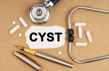 Tıp ve sağlık konsepti. Masanın üzerinde steteskop, haplar, üzerinde CYST yazan bir kalem ve kağıt var.