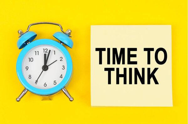 Концепция бизнеса и финансов. На желтом фоне лежат часы и наклейка с надписью - ВРЕМЯ ДУМАТЬ
