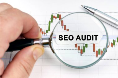 Ekonomi konsepti. Bir adam, üzerinde SEO AUDIT yazan dosya ve kağıda büyüteç ile bakar.