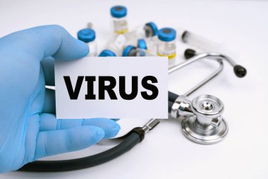 Tıp ve sağlık konsepti. Bir stetoskop ve ampuller beyaz arka planda yatar, doktor üzerinde VIRUS yazan bir kartvizit tutar.