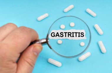 Tıp ve sağlık konsepti. Bir adam büyüteçle haplara ve üzerinde GASTRITIS yazan bir yaprağa bakar.