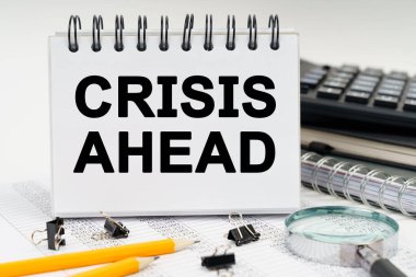 İş ve ekonomi kavramı. Masanın üzerinde bir büyüteç, kalemler, günlükler ve üzerinde CRISIS AHEAD yazan bir defter var.